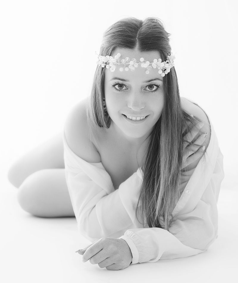 Foto de estudio de Laura Casas tumbada en el suelo con una camisa blanca y una diadema de piedras.